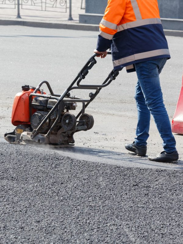Vertical shot of a road worker repairing a stretch of a road on a sunny day